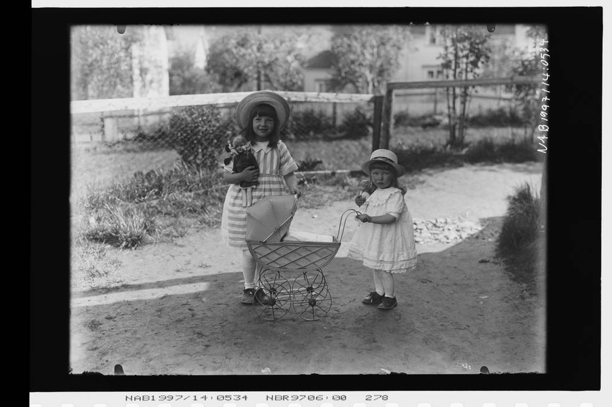 To små jenter med barnevogn (dukkevogn) ute i hagen