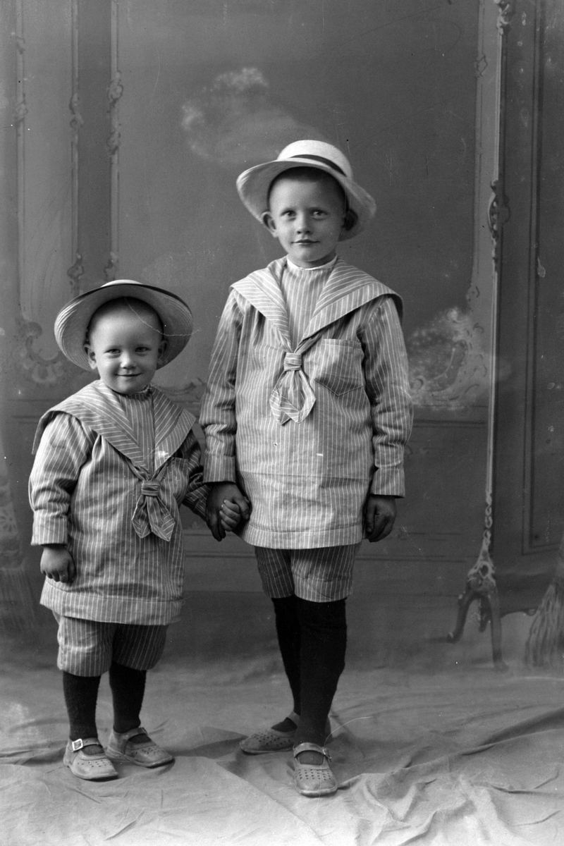 Studioportrett av to små barn med hatter på hodet.