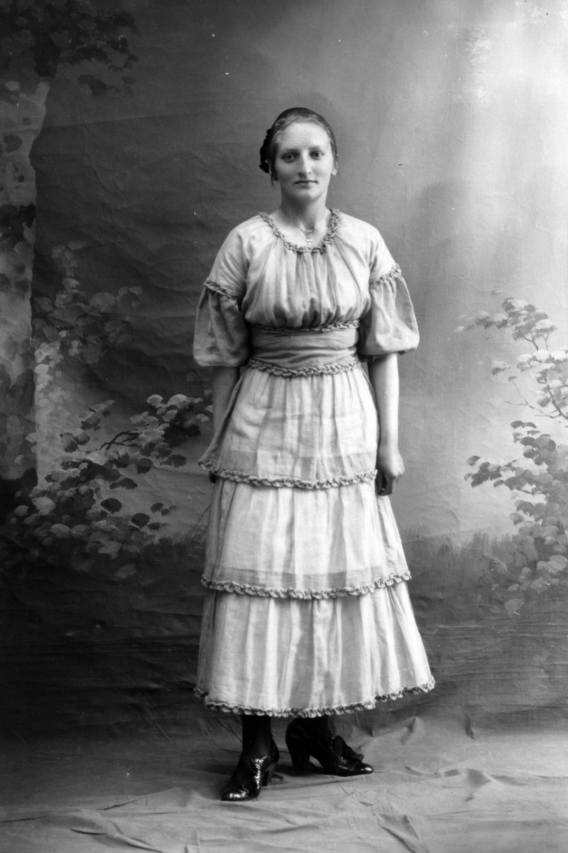 Studioportrett av en kvinne i en lys kjole.