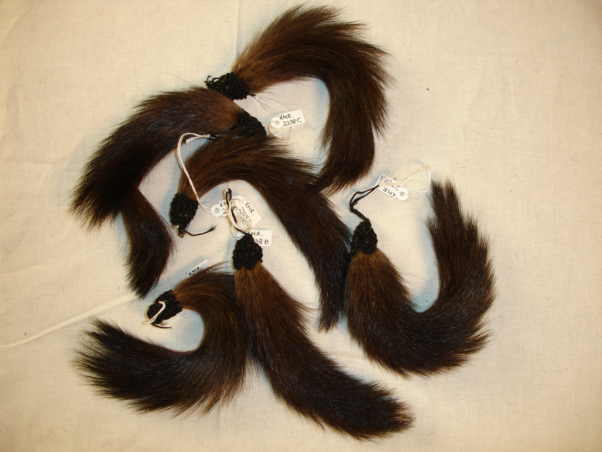 Draktpynt, stykker av pels. 6 stykker laget av hale av pelsdyr, trolig mink. Endestykkene er i makramelignende snorteknikk.