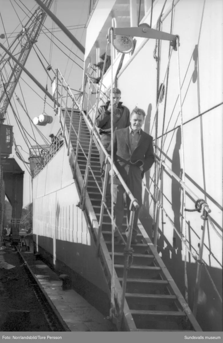"En sjöman går i land" - reportagebilder för Östersundsposten. Fartyget Annie Johnson, ligger vid kaj i Sundsvall och några sjömän passar på att utforska staden. Konditoribesök, torghandel, ölcafé, utsikten från Norra berget, skrivande av vykort, biografbesök.