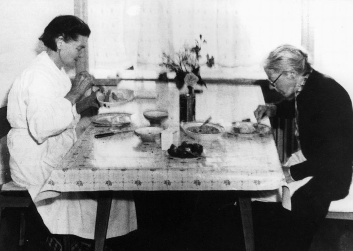 Dorthea Dahl og Simonetta Kildal, begge tjenestefolk i Sortland hovedgård, sitter og spiser ved kjøkkenbordet i Gården.