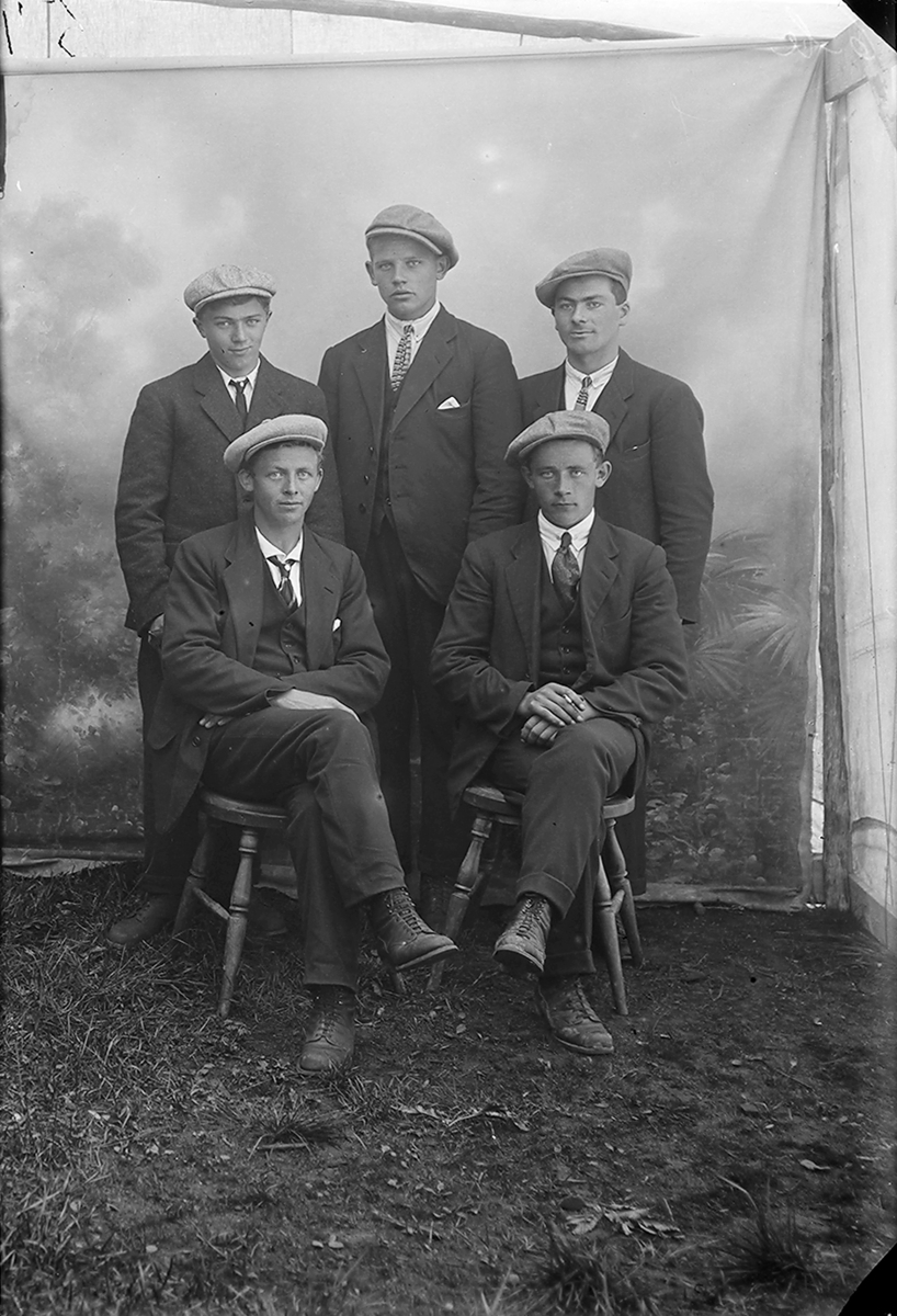 Portrett. Fem mann. To sitter på stoler, tre står bak stolene Alle mennene har på seg dress, slips og lue på hodet. Sørfoldbilde.