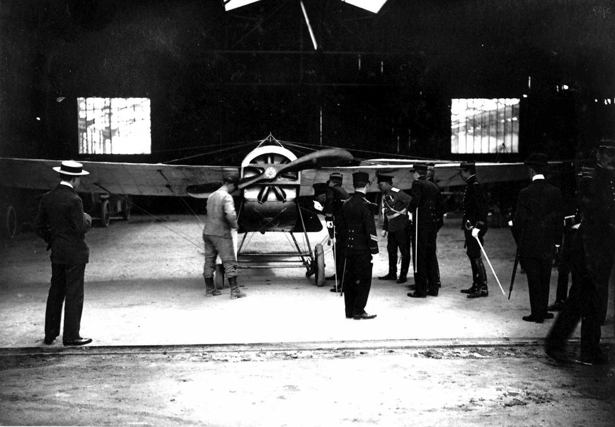 Ett fly, Hanriot DII, inne i en hangar. Flere personer ved flyet.
