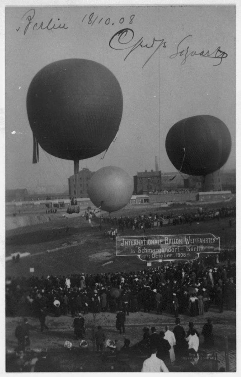 Tre ballonger i lufta. Mange personer på bakkenog flere bygninger i bakgrunnen.