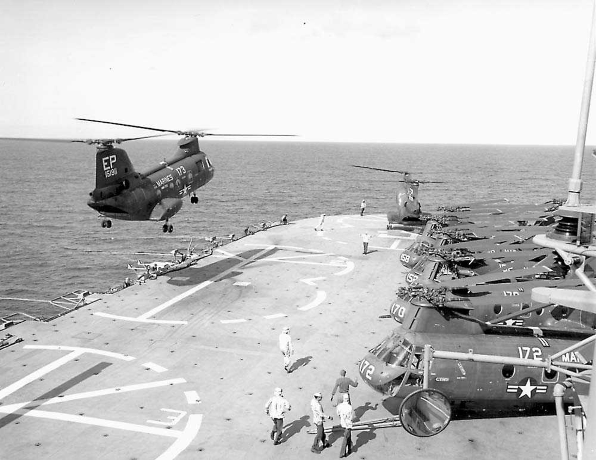 1 helikopter i luften over et hangardekk. Boeing Vertol CH-46 Sea Knight Flere helikoptere og personer på dekk.