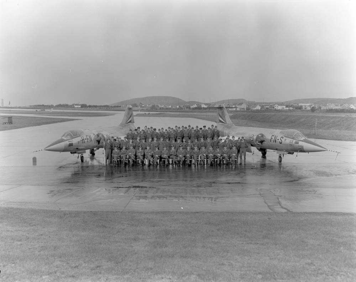 Gruppefoto av personellet ved 331 skvadron på Bodø flystasjon. På hver side av personellet er plassert en F-104 Starfighter og i bakgrunnen sees deler av Bodø by. På første rekke, nr. 8 fra venstre, sees Skvadronssjef Major Olav F. Aamoth.