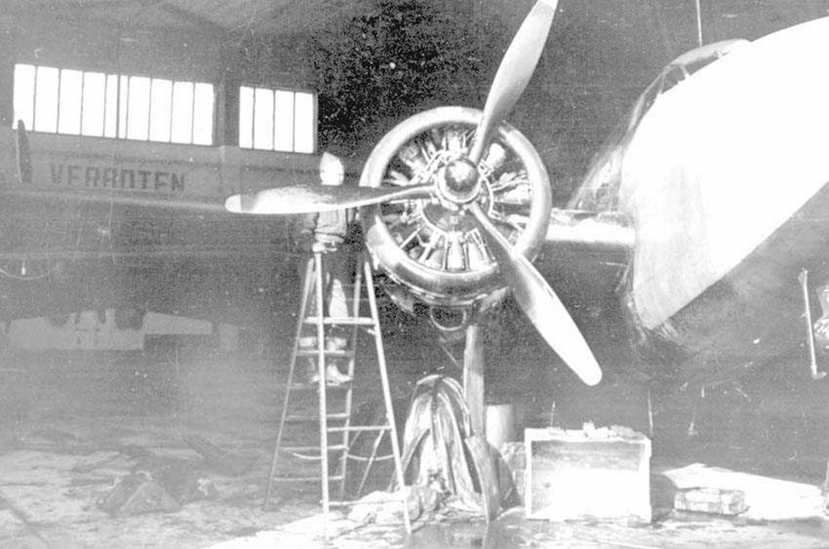 Et fly som står i en hangar. En person som står på en gardintrapp ved propellen.