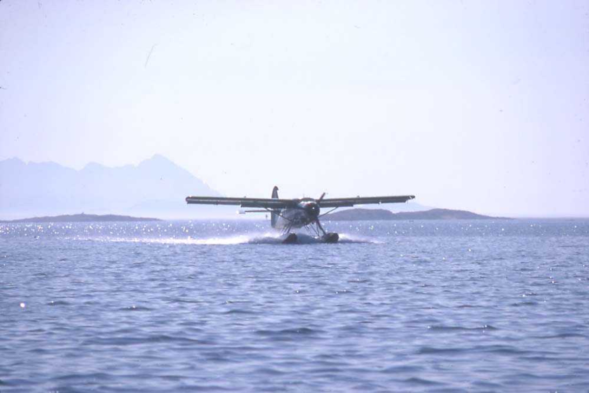 Ett fly i fart på vannet, DHC-3 Otter LN-BDD fra Widerøe. Fjell i bakgrunnen.