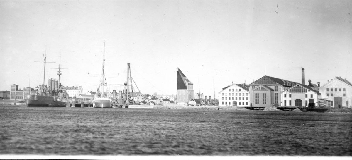 Ingenjörsdepartementets verkstäder med Pansarskeppet Fylgia och övningsfartyget Chapman vid utrustningspiren. Pansarskeppet Oscar II och torpedkryssaren Jacob Bagge på vänster sidan.