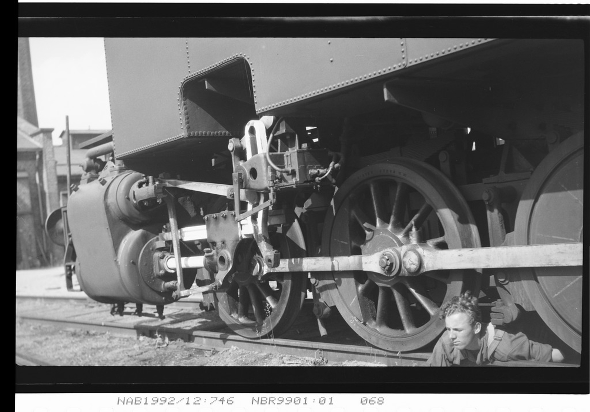 Mann ligger mellom hjulene på et lokomotiv.