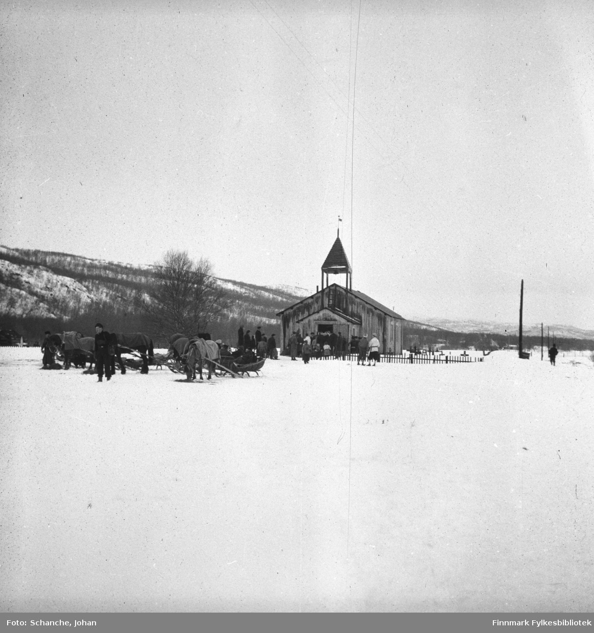 Polmak kirke fotografert på påsken -46. Utenfor kirken står hester med sleder. Folk er på veg til kirken. Bildet er tatt fra lang avstand.