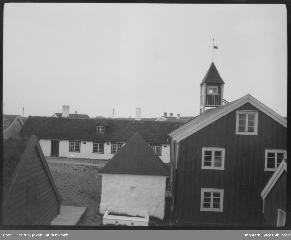 Bygninger på Vardøhus festning.  Det lille hvite huset midt i bildet er aggregathuset, opprinnelig brønn.  Huset med tårn er depotet ('proviant- og materialhus').  I bakgrunnen med torvtekt tak og arker garnisonsbrakken, også kalt kasernen eller 'slaveriet'.