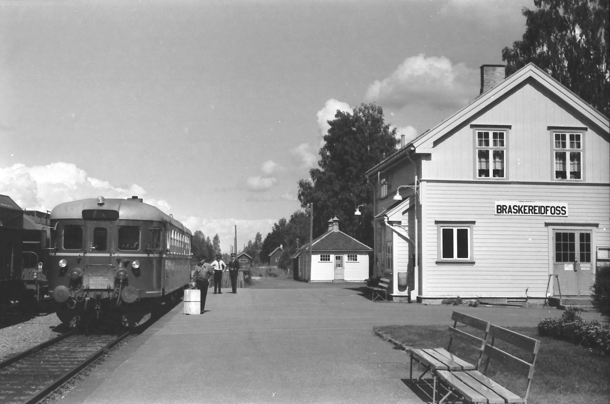 Tog fra Kongsvinger til Elverum og Hamar stopper i Braskereidfoss. Utvendig stasjonsbetjent lemper gods, mens togfører (overkonduktøren) og tjenestegjørende stasjonsmester (txp) samtaler.