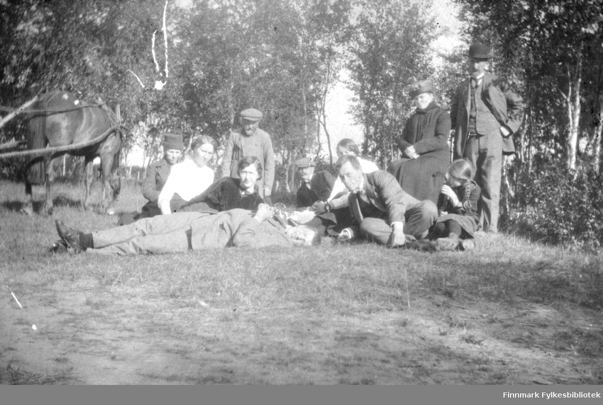 Elleve mennesker fotografert på en gressplen en solfylt dag i august 1916 i Rasjok i Tana. Av dem er fem kvinner, fem menn og en jente. Jenta til høyre i bildet er 10 år gamle Gullen (Gudrun) Andersen, senere Borchgrevinck. I midten foran sitter Hans Gabrielsen. Til venstre står det en hest som er spent fast i en vogn som ikke sees.