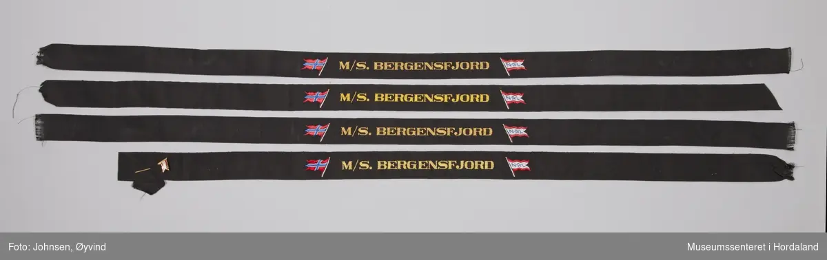 Sort luebånd M/S. Bergensfjord med det norske flagget og NAL flagget. På båndet er det festet en pyntenål med NAL flagget.