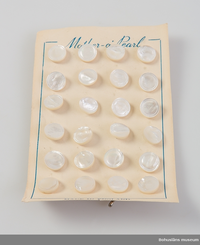 En uppsättningar med 30 fastsatta skjortknappar av vit pärlemo fastsatta mot kartongblad. På framsidan tryckt text:
Mother - o -pearl samt MADE IN ENGLAND.
Knapparna har en yttre dekorrand i relief. På baksidan ögla med rostfri klammer.