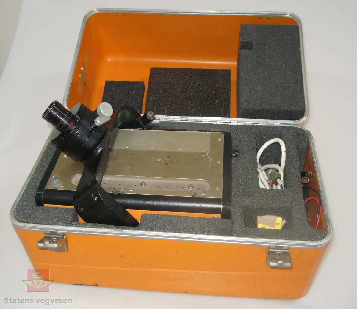 Oransje og svart elektronisk avstandsmåler med tilhørende utstyr og bruksanvisning, i oransje oppbevaringskasse. Merking.