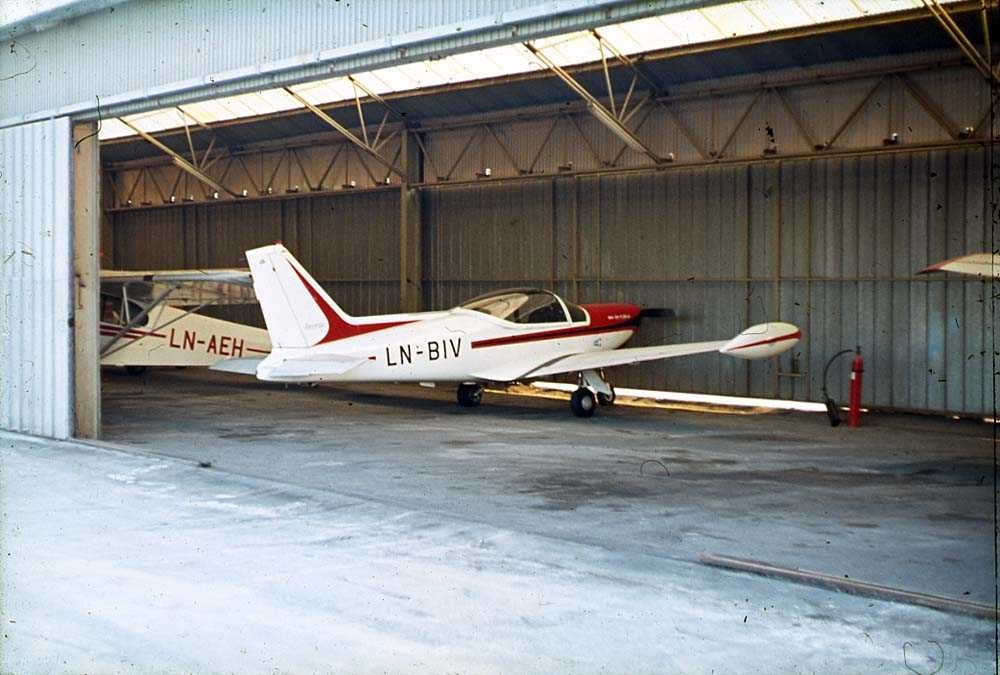 Ett fly inne i en hangar, SIAI-Marchetti SF.260 LN-BIV. Ett annet fly i bakgrunen.