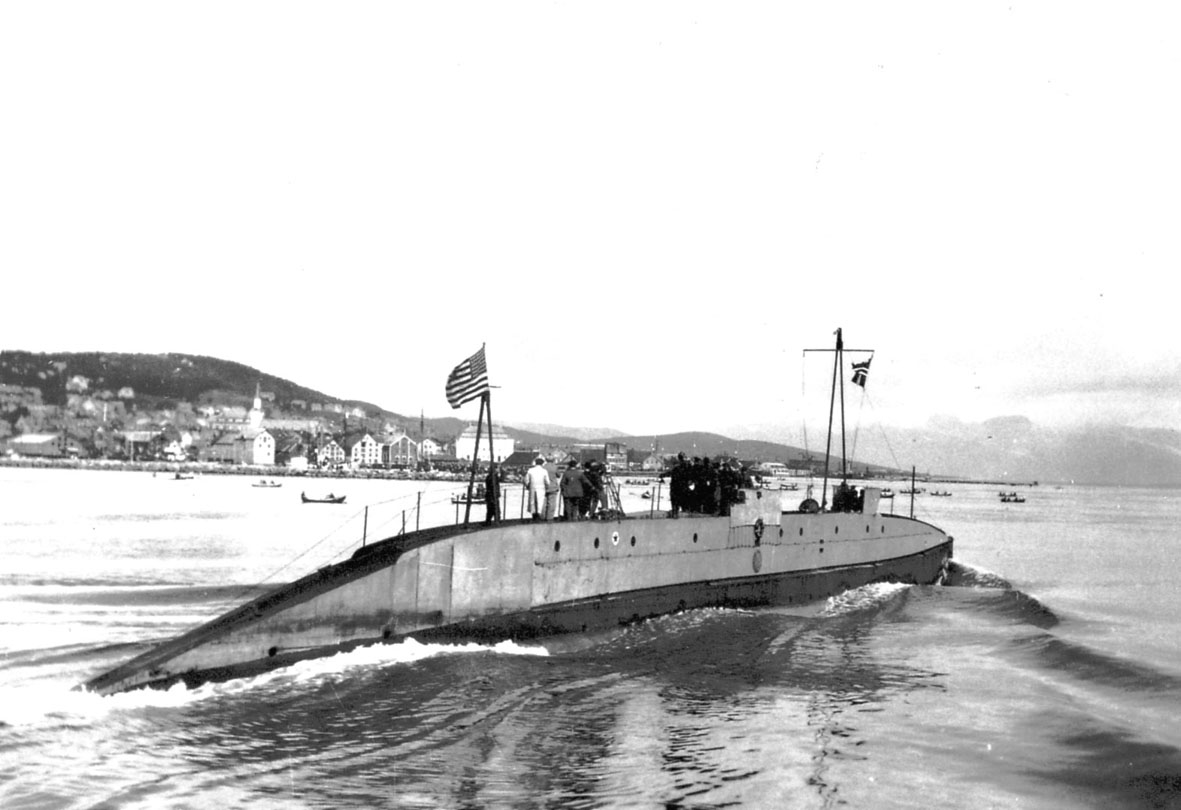 Ubåten "Nautilus" i sakte fart, bebyggelse bak, bl.a. ei kirke. 