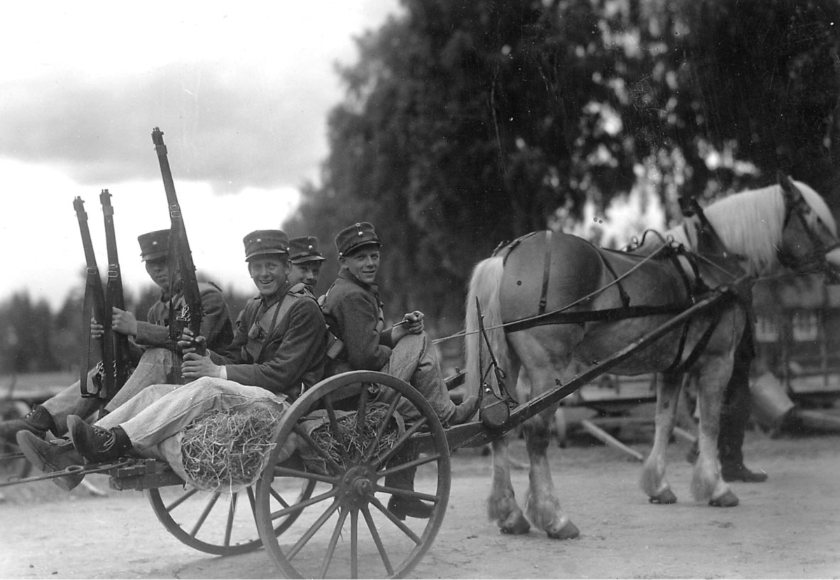 Hest og kjerre, fire personer, soldater med geværer  sitter på hestevogna.