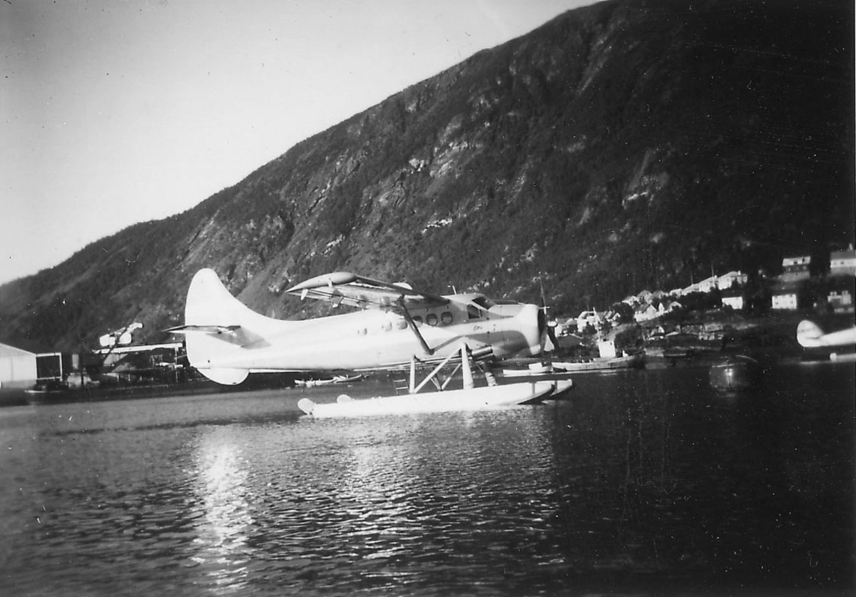 Sjøflyhavn, ett fly på vannet, De Havilland, Otter, fortøyd i bøye. Kaianlegg, flere båter og bygninger i bakgrunnen.