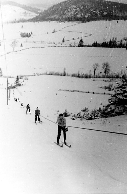 Snødekt skråning, flere personer på ski blir trukket oppover av skitrekk. 