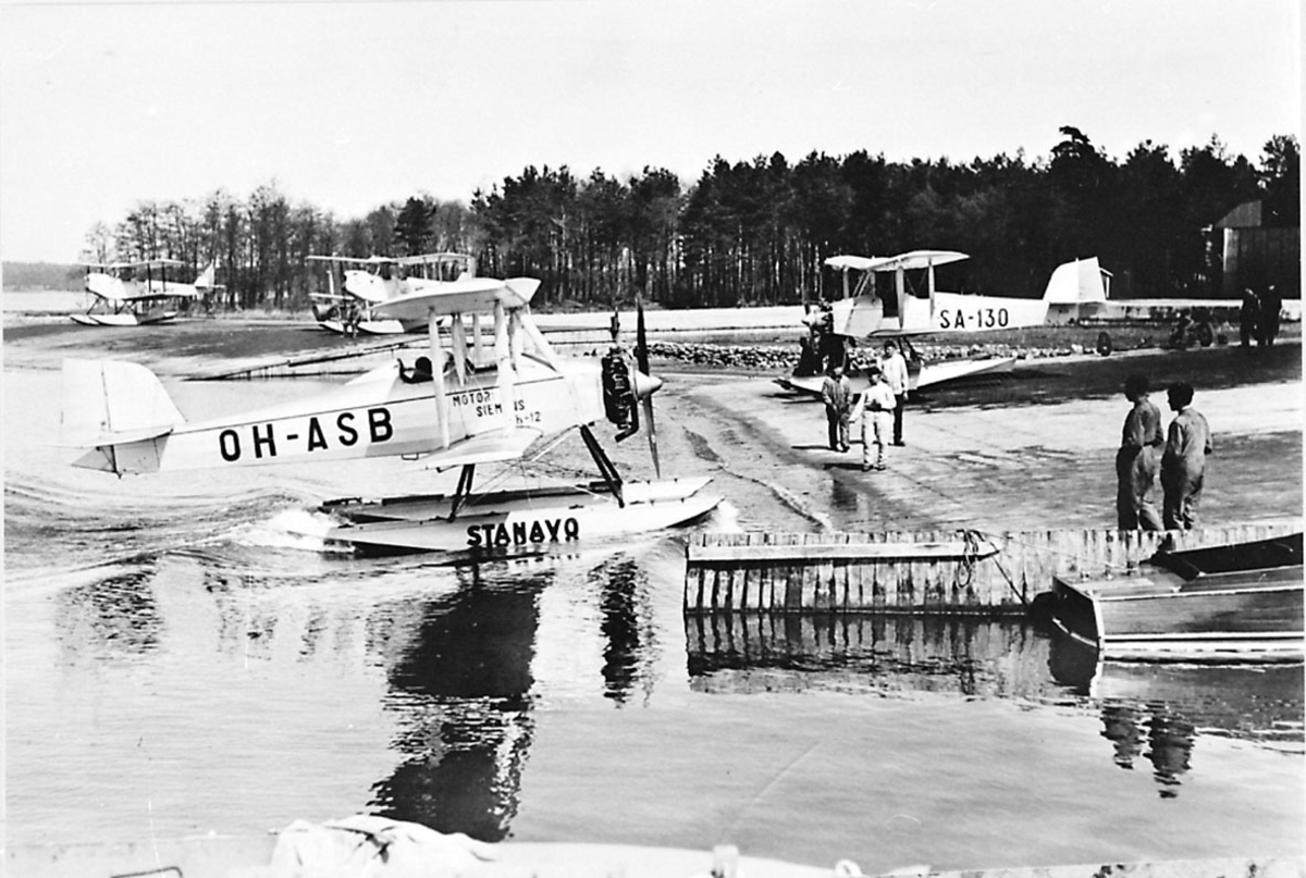 Fly, propellfly, dobbeldekker, Sääski OH-ASB, foran. Sjøflyhavn med flere sjøfly. Noen personer. 