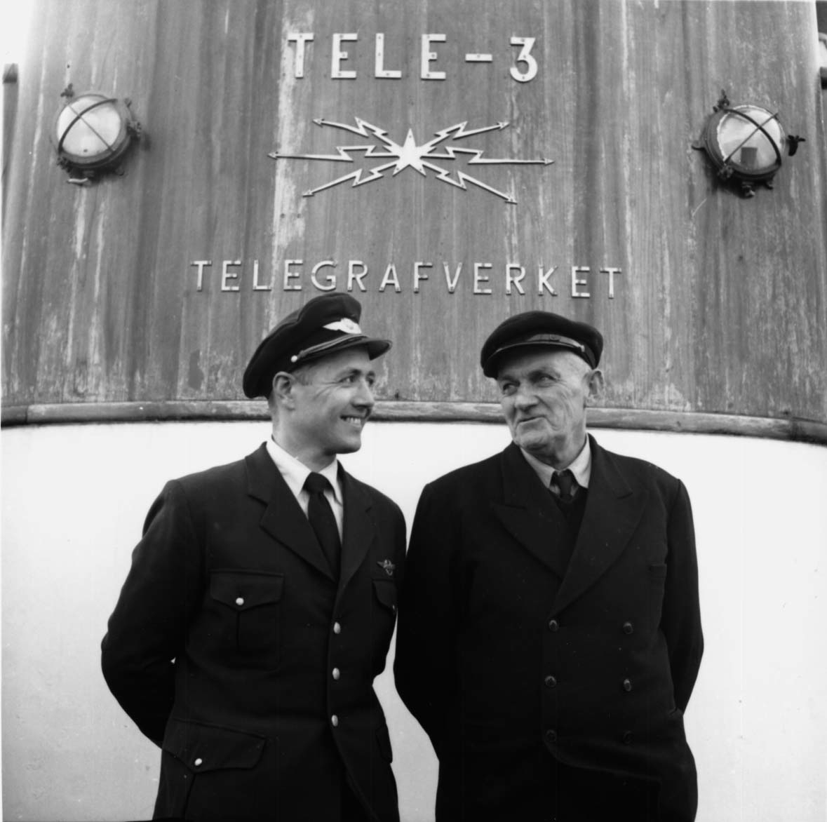 Portrett, 2 personer står foran ei bygning med påskrift "Telegrafverket".