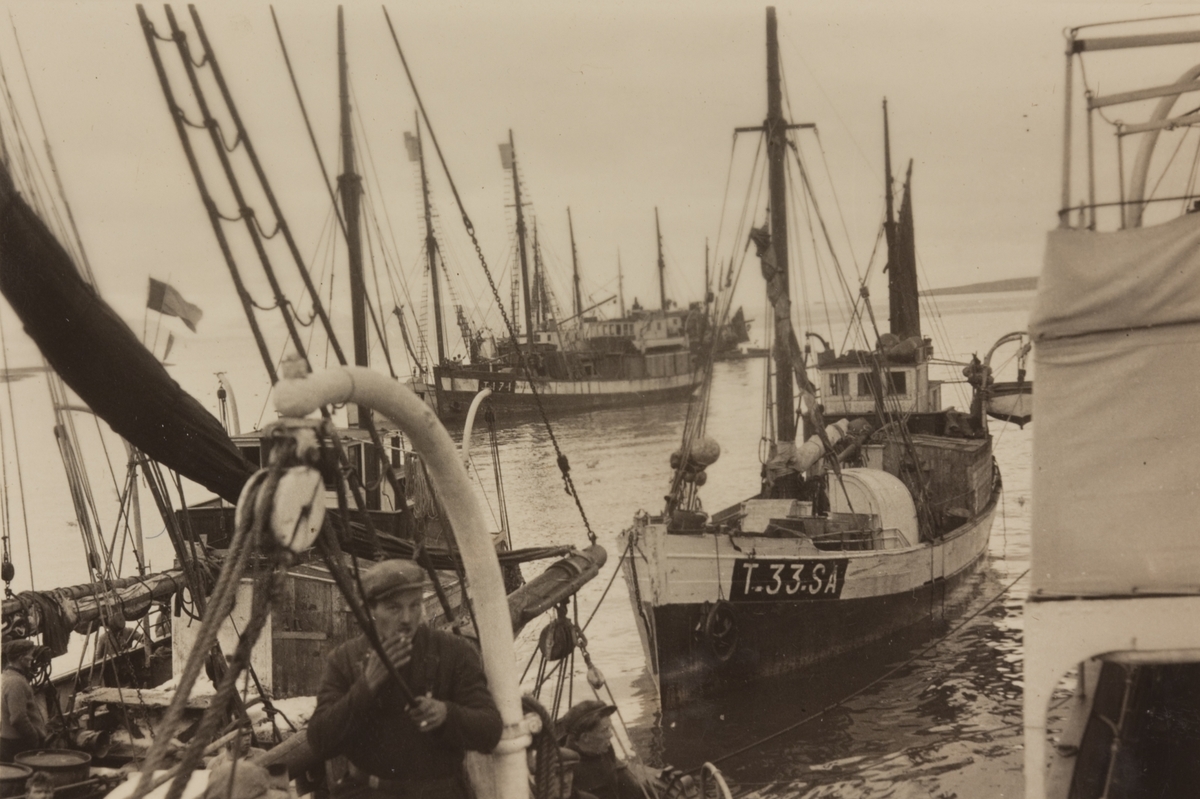 Fiskekuttere i en havn. Mann med sigarett i forgrunnen.