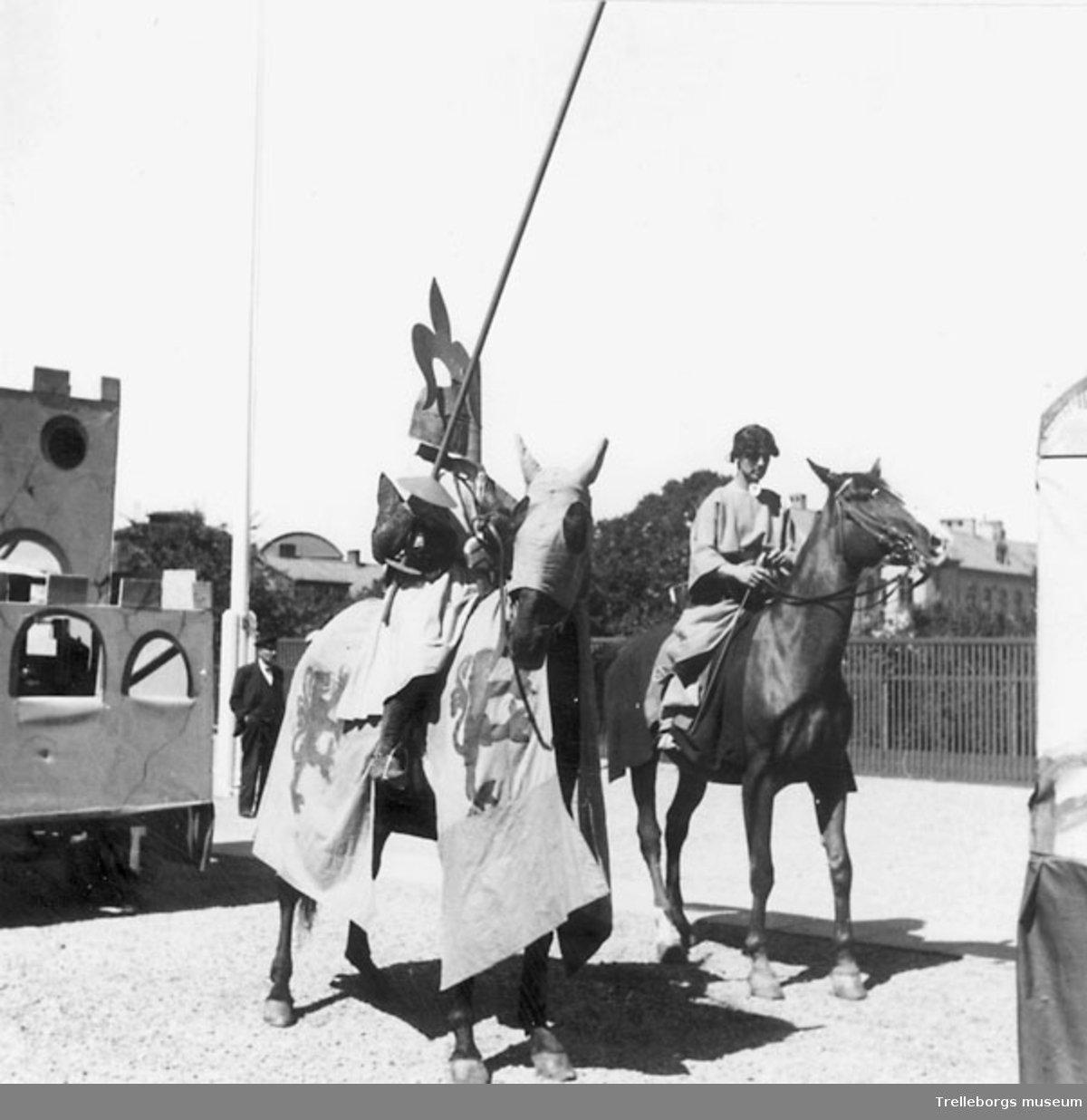 Torgfesttåget 1937. Två män till häst föreställande en medeltid riddare i full utstyrsel och hans tjänare. Bakom dem en karnevalsvagn som föreställer en borg. Negativ 70:1327.