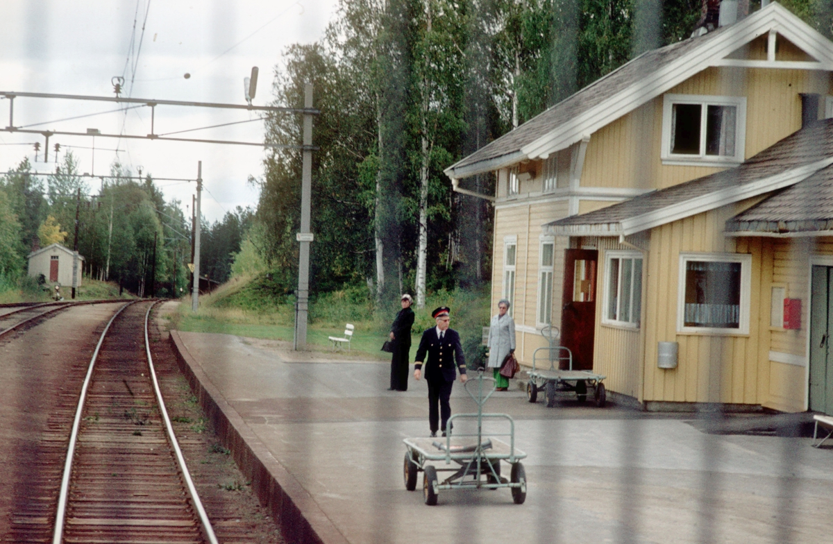 Persontog fra Oslo Ø kjører inn på Nygard stasjon, sett fra lokomotivet. Togekspeditør på plattformen og reisegodstralla står klar. Et par reisende til Gjøvik venter på toget.