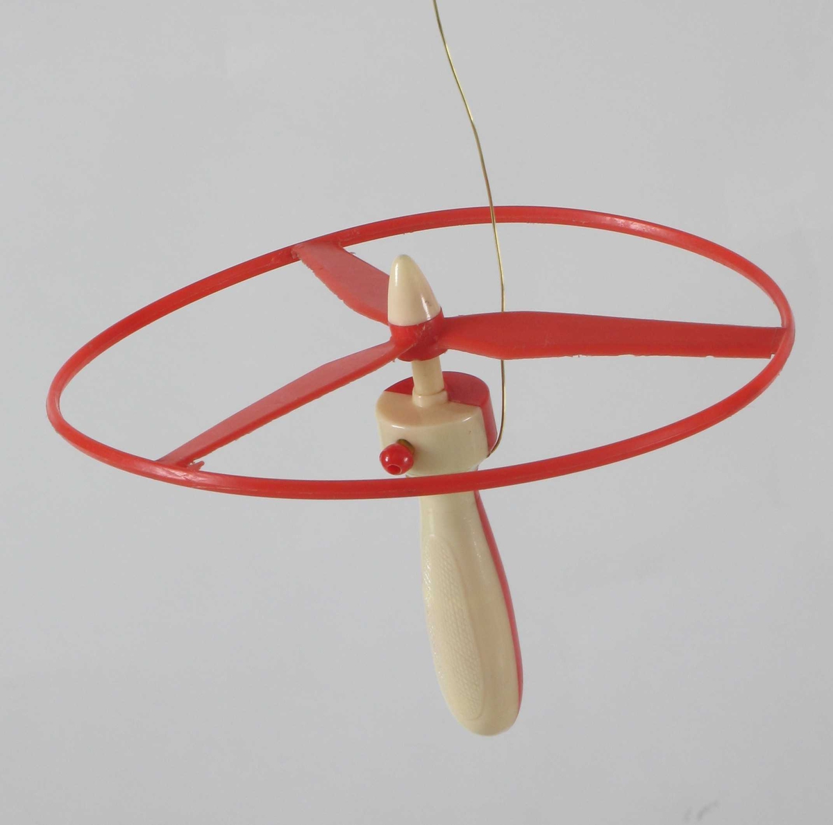 Propell i tynn plastsirkel. I midten et hull, settes på håndtaket som har en snelle med kule i enden til å trekke opp propellen med.  Rød propell, rødt og beige håndtak.