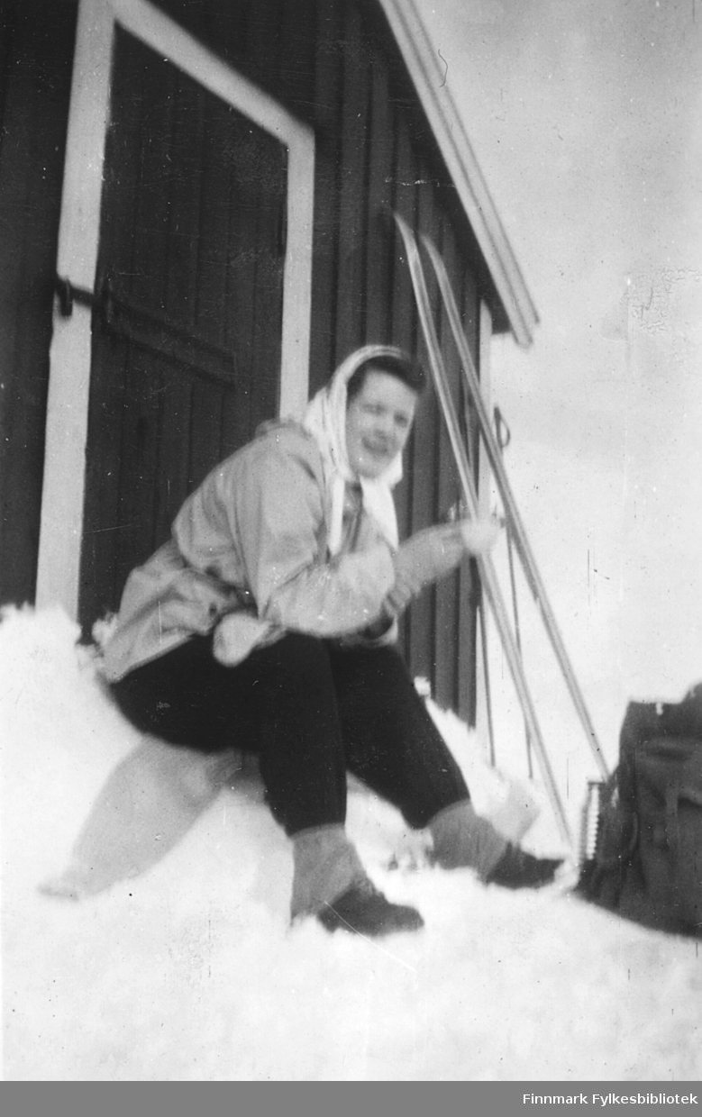 Ragnhild Ebeltoft på skitur, Vadsø-området, 1950-tallet. Her raster hun på ei hyttetrapp. Skiene står stilt opp mot veggen, ryggsekk og termos står i snøen foran henne