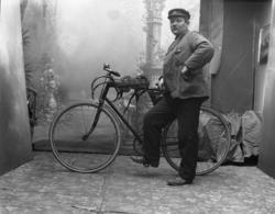 Mann med sykkel i A.F. Johansens atelier. På sykklen henger 