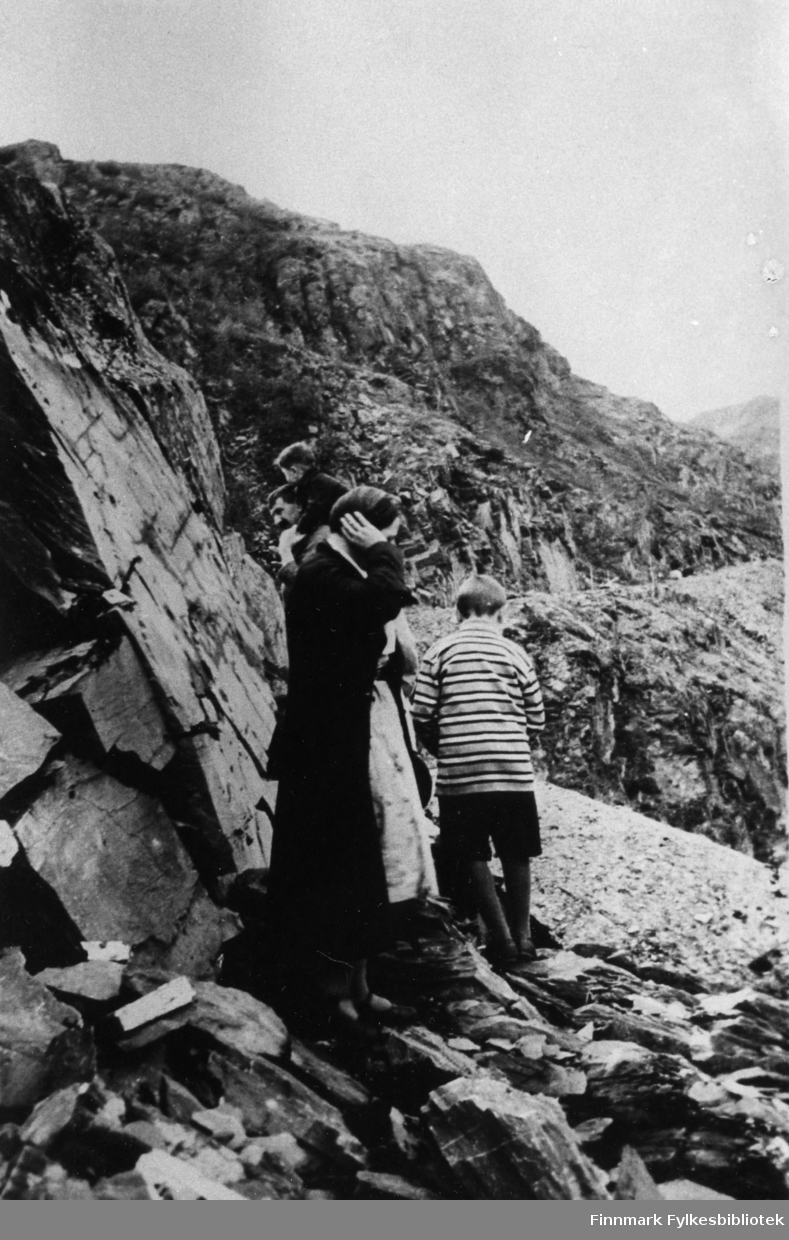 Fjellskjæringen utenfor Sjursjok. Her ser vi Fixdal med minste barnet på skuldrene etter ham går en annen av hans sønner og til sist en kvinne. De går langs skjæringen i fjellet.