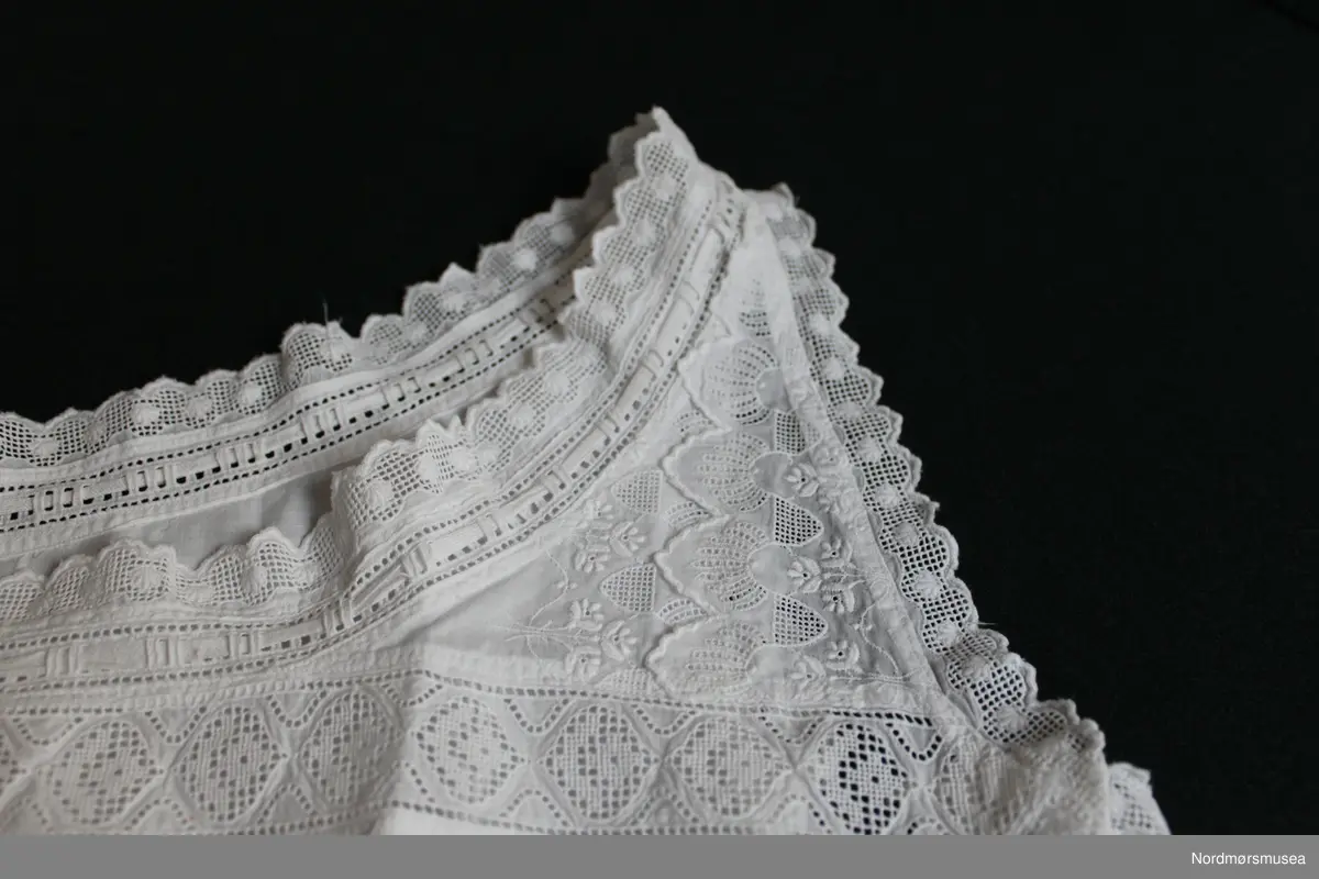 Kort liv. Undertøy til dame. Figursydd. Knapper i venstre side, 6 stk. Innfelte blondebånd, fra brystet og opp. Knytebånd ved avslutning mot hals.