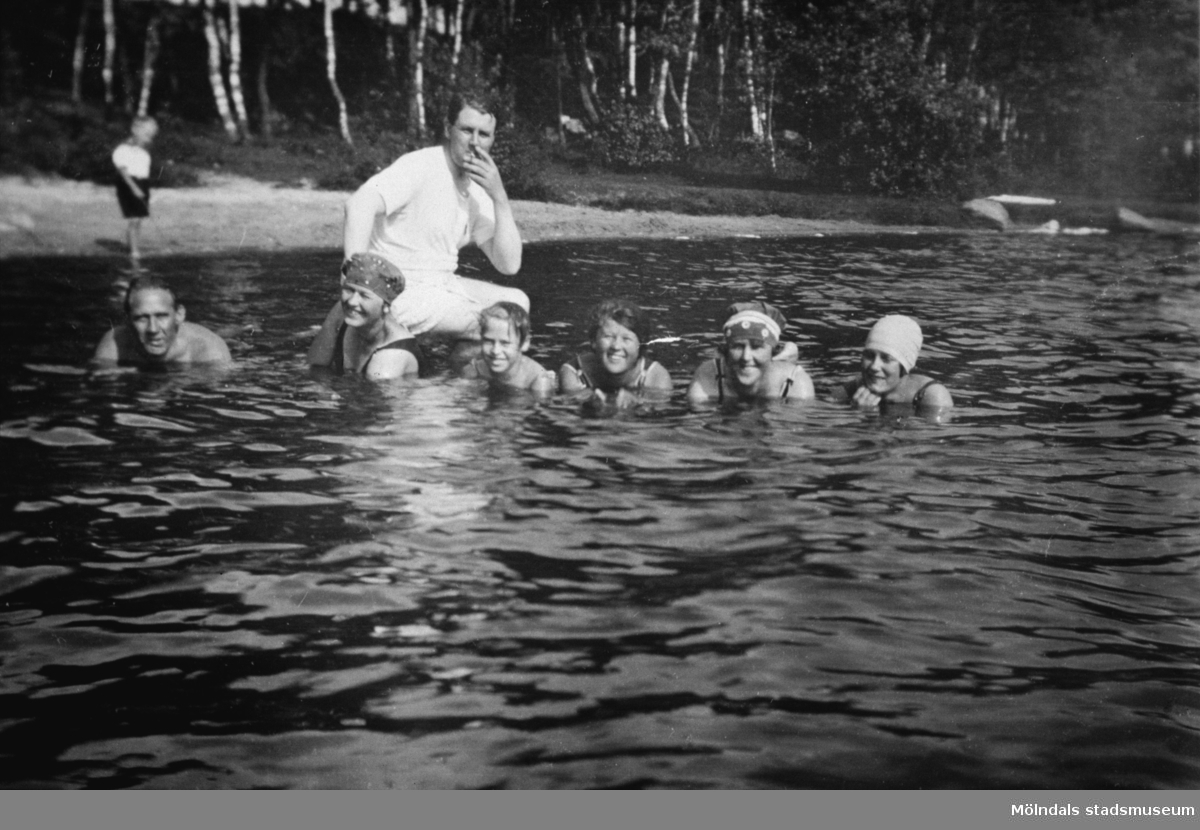 Några personer badar i Tulebosjön, 1930-tal. Det är antingen familjen Alberts eller sommargäster. I bakgrunden till höger ses en strand och träd.