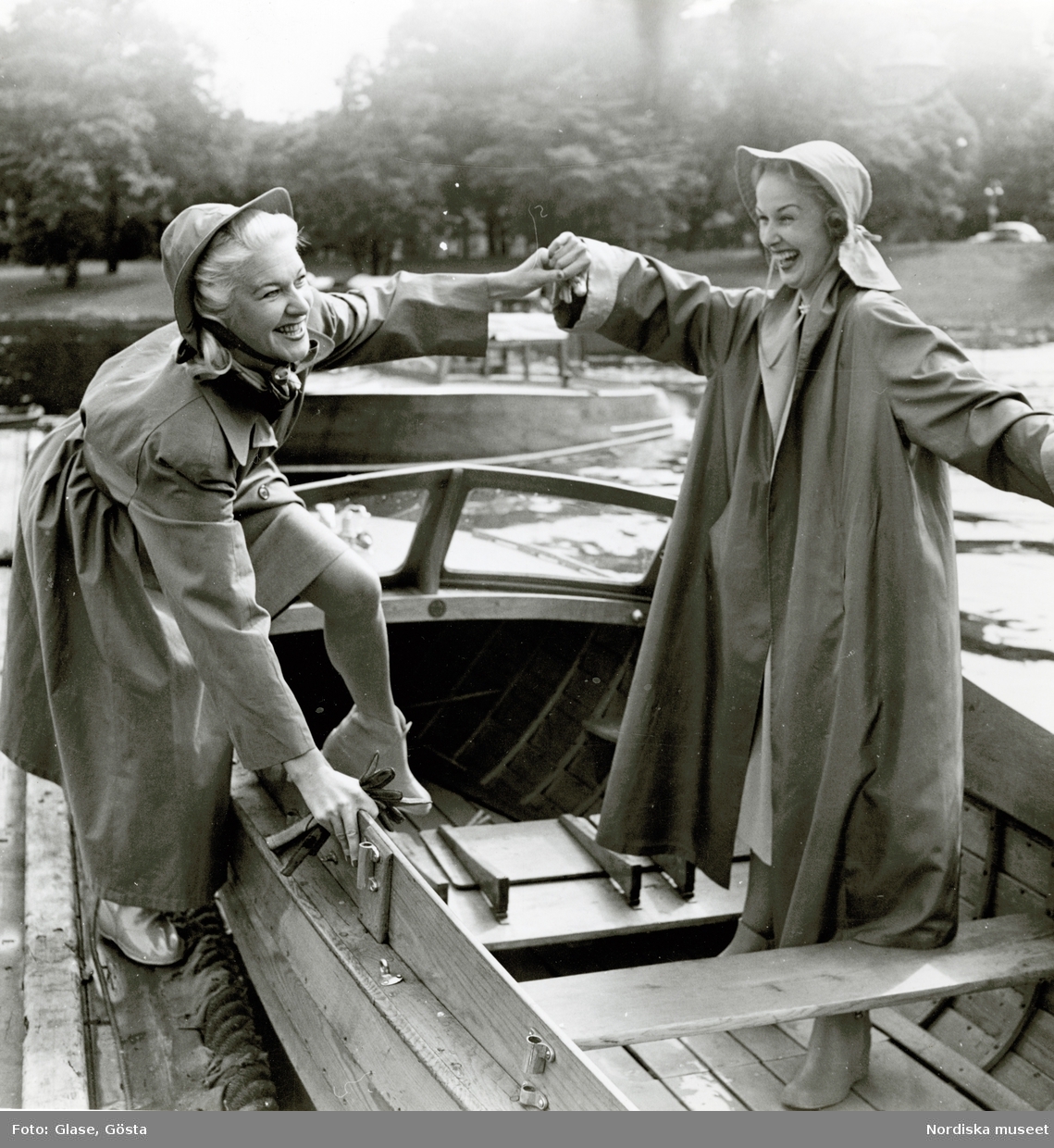 Två kvinnor i regnkappor och regnmössor i en båt.
