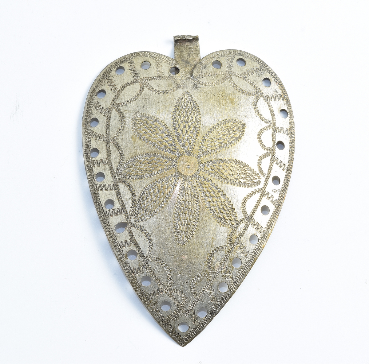 Tynn, hjerteformet spenne i sølv dekorert med en siselert blomst med åtte kronblader. Spennen er gjennomhullet på kanten.