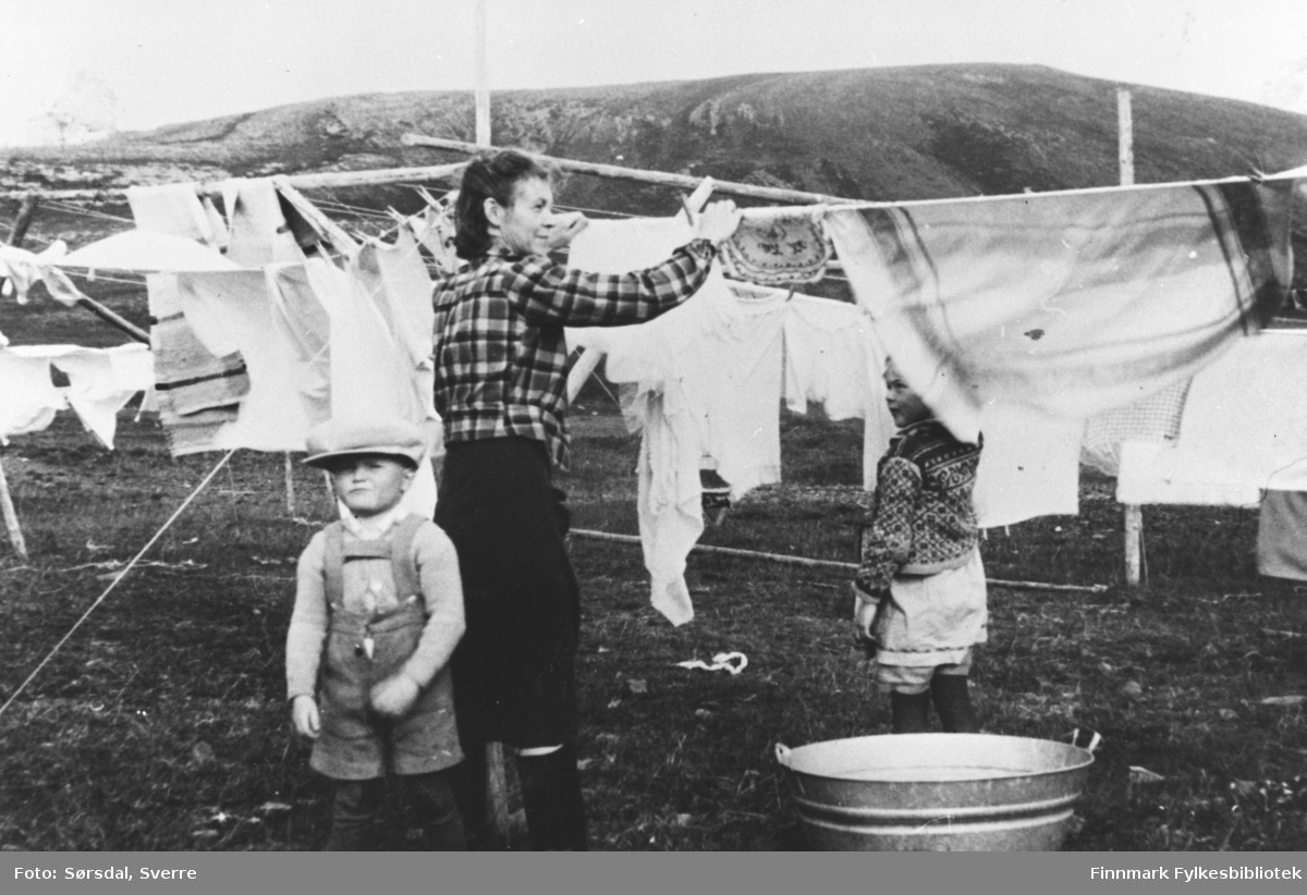 Else Sørsdal henger klær til tørk mens familien bodde i Syltefjord. Else var gift med overlegen på Vardø sykehus, Sverre Sørsdal. Sykehuset ble bombet og brant ned til grunnen 1. mars 1942. Etter noen urolige måneder ble det avgjort å flytte til Syltefjord, hvor internatet ble tatt i bruk som provisorisk sykehus. Barna på bildet er Randi og Eirik Sørsdal