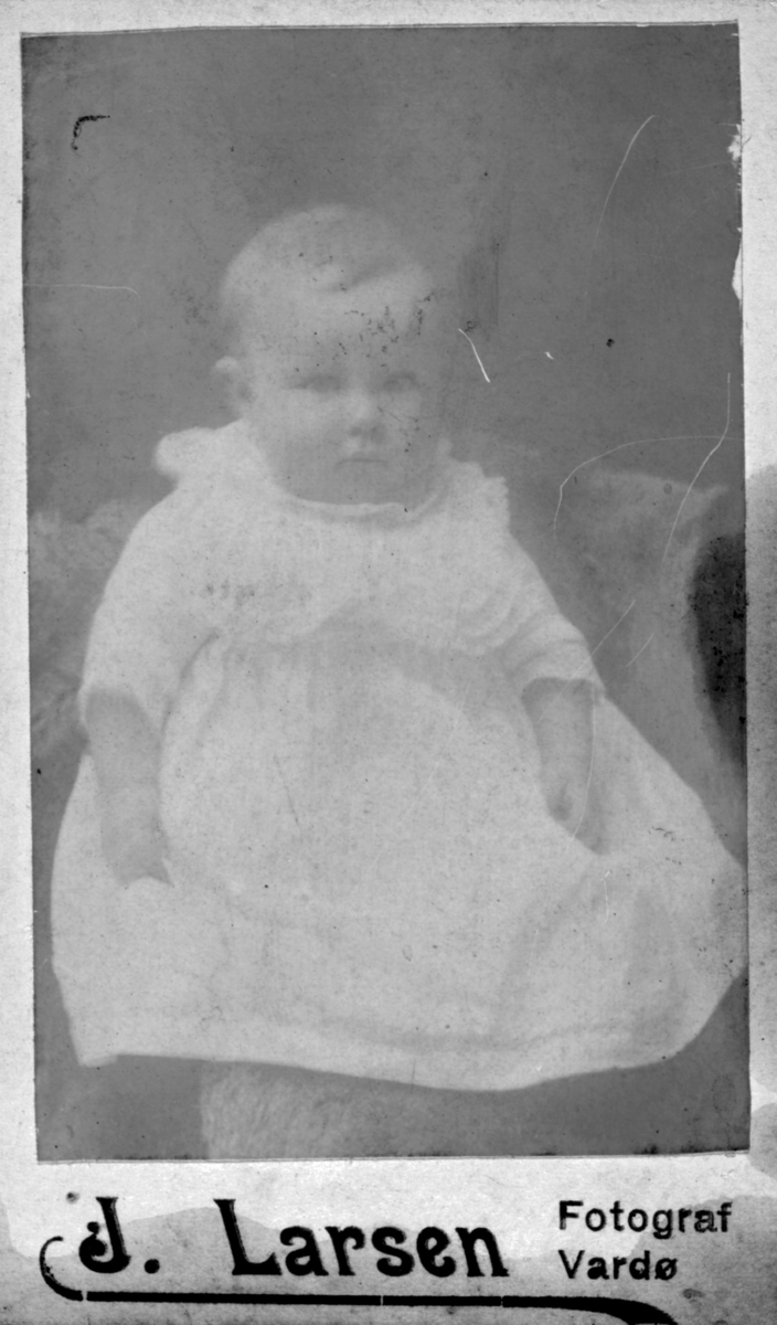 Et spedbarns portrett. Ingen opplysninger. Barnet har på seg en kjole. Bildet trolig tatt på slutten av 1800-tallet, begynnelsen av 1900-tallet.