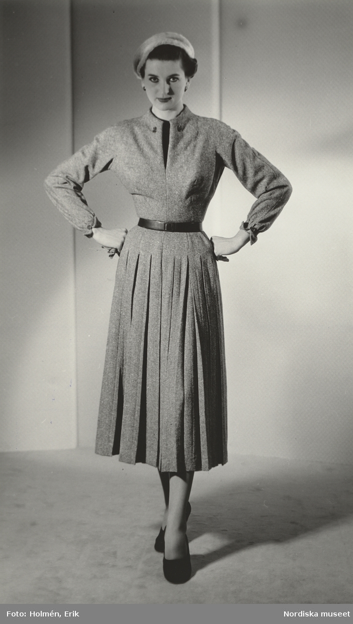 Modell i ylleklänning med veck nedtill, skärp och hatt. Från Dior.