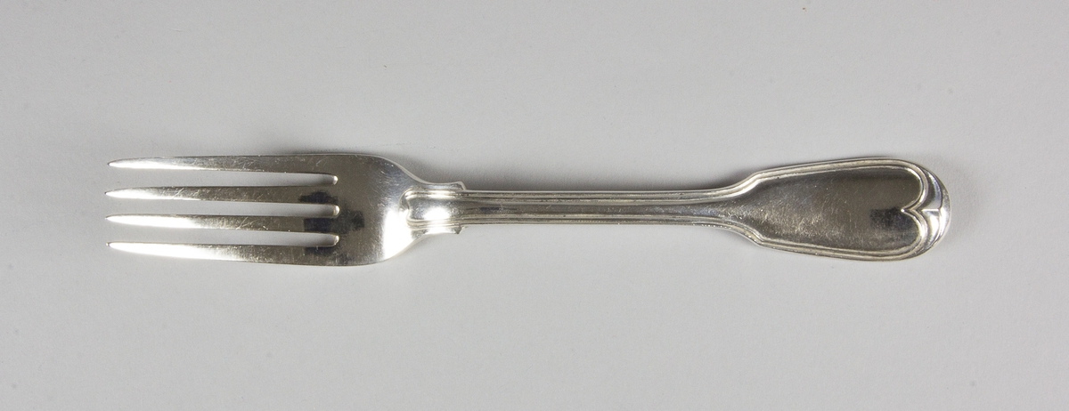 Gaffel av silver med fyra klor. På skaftets ovansida löper en kant som i övre änden avslutas i en hjärtformad spets. Med stämplar på skaftets baksida.