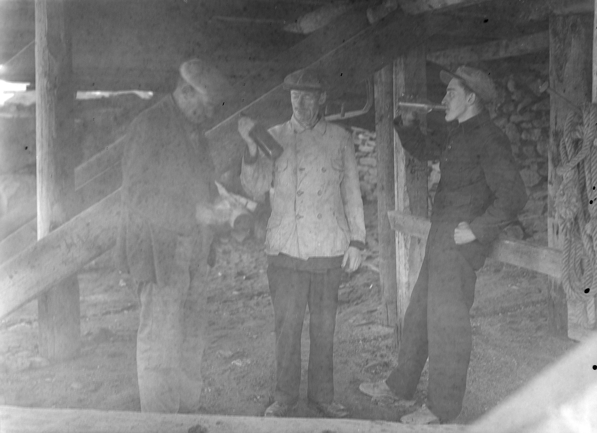 Tre menn drikker brennevin under ei brygge