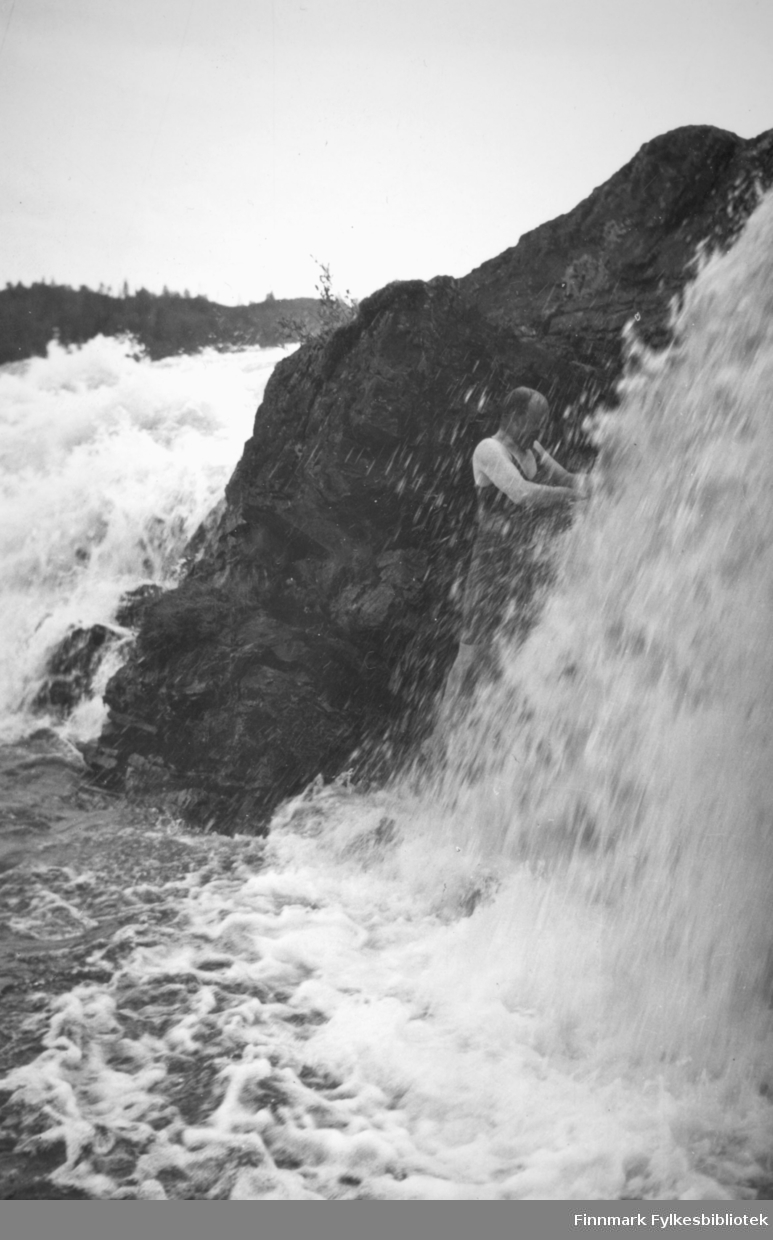 Fra Adamsfossen, person ukjent.  Bak fotografiet står det skrevet: "Morgendusj under Skogfoss, Pasvik, 1938". Bildet er fra Nord-Norges Turisttrafikk-Forbund, Harstad. Foto: ukjent.