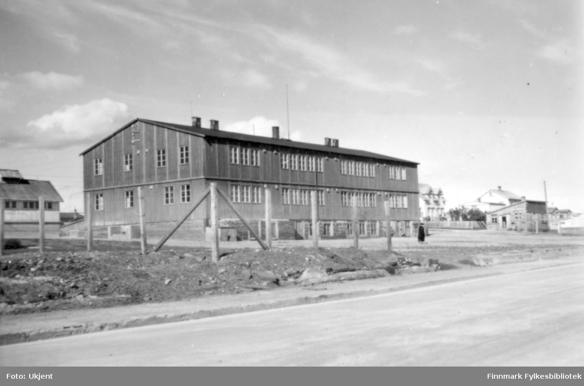 Skolebrakka, som ble satt opp i 1946 på grunnmuren til den gamle Folkeskolen, og som hadde klasserom for både folkeskolen og realskolen i Vadsø. Til høyre brakka der Johan Grønvigh hadde sine forretning. Foto: ukjent.
