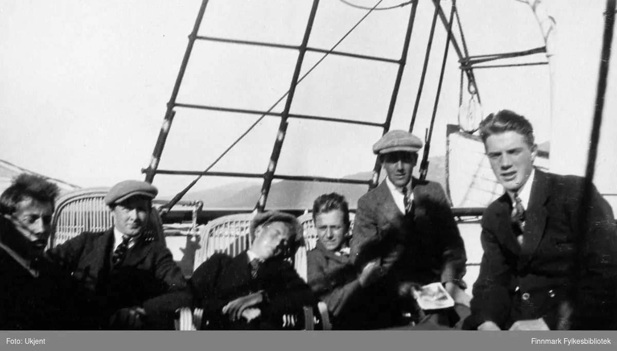 Her poserer en gruppe med gutter ombord et skip som trolig er Hurtigruten. Alle guttene er ukjente. De fleste av dem sitter på stråstoler. Tre av guttene har på seg luer, nummer fem fra venstre holder et magasin eller en bok i hånden. Guttene har på seg slips, jakke og bukser. Bak dem til høyre kan man se en livbåt og bak livbåten kan man se fjell.