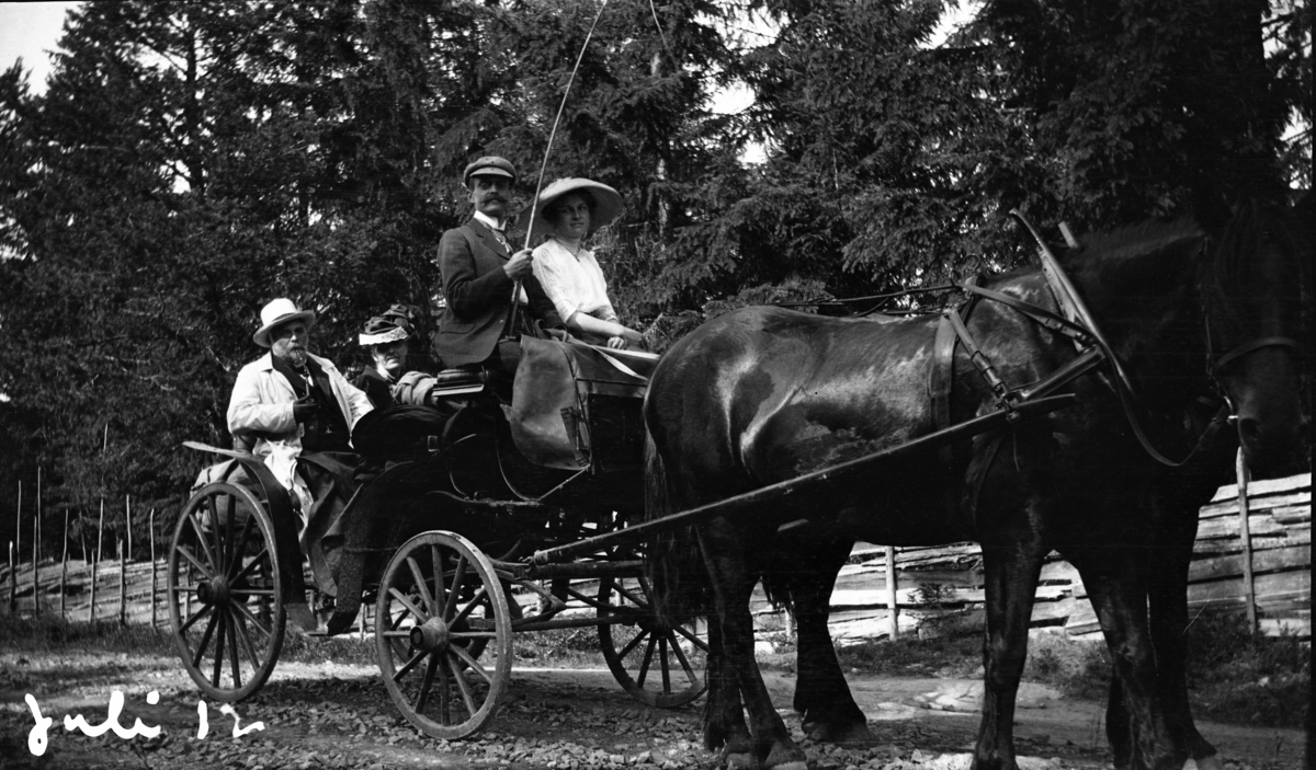 Fotoarkivet etter Gunnar Knudsen. To hester som drar en vogn med fire mennesker i. Bildet er tatt juli 1912