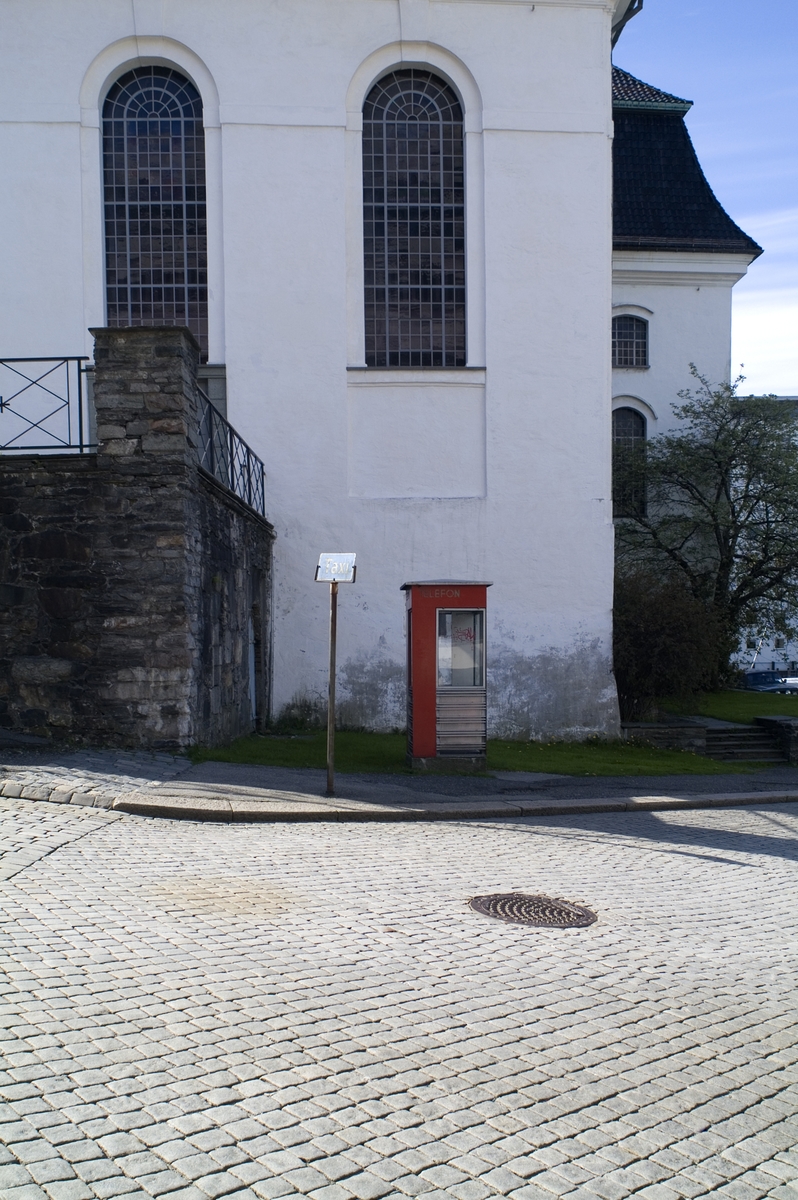 Telefonkiosken står ved Nykirken i Bergen, og er en av 100 vernede telefonkiosker i Norge. De røde telefonkioskene ble laget av hovedverkstedet til Telenor (Telegrafverket, Televerket). Målene er så å si uforandret. 
Vi har dessverre ikke hatt kapasitet til å gjøre grundige mål av hver enkelt kiosk som er vernet. 
Blant annet er vekten og høyden på døra endret fra tegningene til hovedverkstedet fra 1933.
Målene fra 1933 var:
Høyde 2500 mm + sokkel på ca 70 mm
Grunnflate 1000x1000 mm.
Vekt 850 kg.
Mange av oss har minner knyttet til den lille røde bygningen. Historien om telefonkiosken er på mange måter historien om oss.  Derfor ble 100 av de røde telefonkioskene rundt om i landet vernet i 1997. Dette er en av dem.